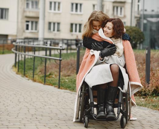 disabled woman in wheelchair with daughter. family walking outside at park